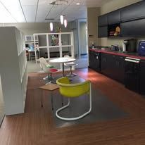 Modern office kitchen with tables, chairs, and black cabinets; a yellow chair is in the foreground.