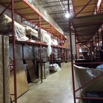 Interior of a warehouse with shelving units loaded with packaged items, viewed down the aisle.