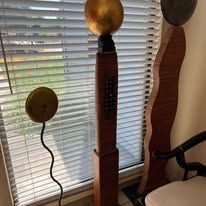 Sculptures stand by a window with blinds. Gold sphere, brown tower, black wires.