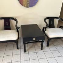 Two black chairs flank a small table on a tiled floor, under a colorful wall hanging.