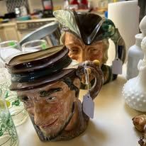 Close-up of two ornate ceramic mugs. One is a man's head and the other with a hat. Indoors.