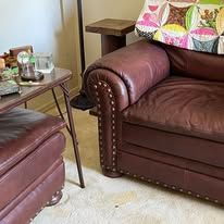 Brown leather couch with decorative studs and a matching ottoman. A small table holds objects.