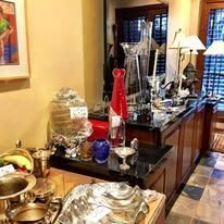 A room with a counter displaying items like vases, glasses, silverware, and decorations for sale.