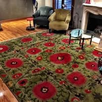 Green rug with large red flower patterns, two chairs and a side table in a room.
