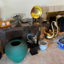 Still life: various objects on a wooden shelf, including a teal vase, golden plate, and metal animals.