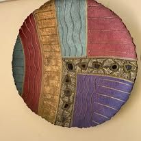 Abstract, circular wall art with textured, colorful sections in red, gold, blue, purple.