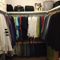 Closet filled with hanging clothes, handbags on shelf. Various colors, wooden hangers.