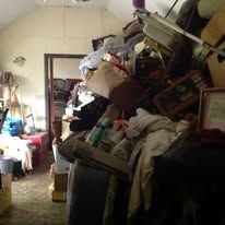 Messy room filled with clutter and items, doorway visible in the background.