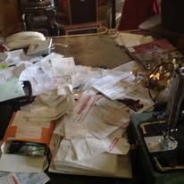 Desk covered in piles of paper, a phone, and office supplies.