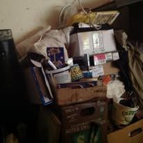 Messy cluttered storage area with boxes, a jar, and other items.