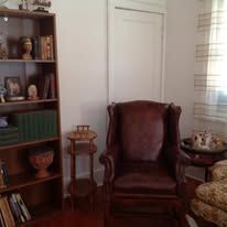 A room with a bookshelf, armchair, side table, and a window, lit by sunlight.