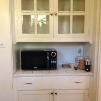 Built-in microwave and cabinets in a kitchen. White doors with glass panels and a tiled countertop.