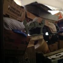 Cluttered storage space with boxes, a fan, and other objects.