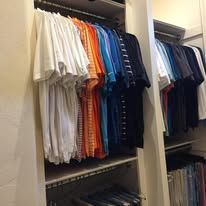 A closet with several rows of colorful shirts hanging neatly, with shelves below.