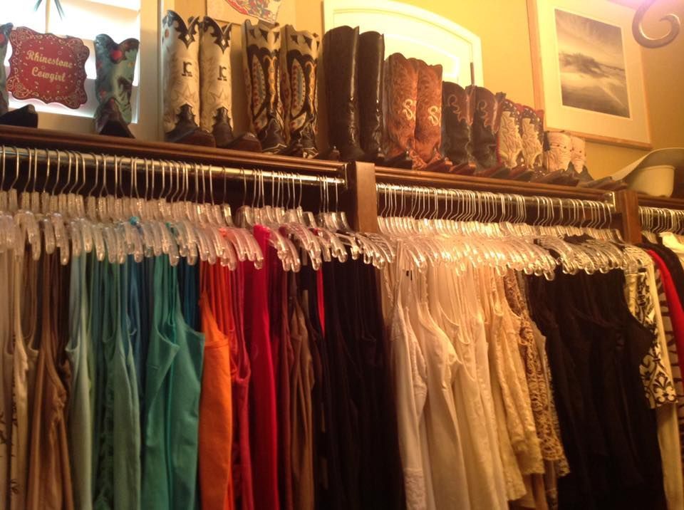 Clothing rack with colorful tank tops, above boots on a shelf.