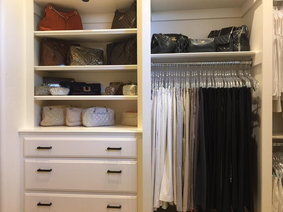 Closet with white built-in shelves holding purses and drawers below. Clothes hang on the right.