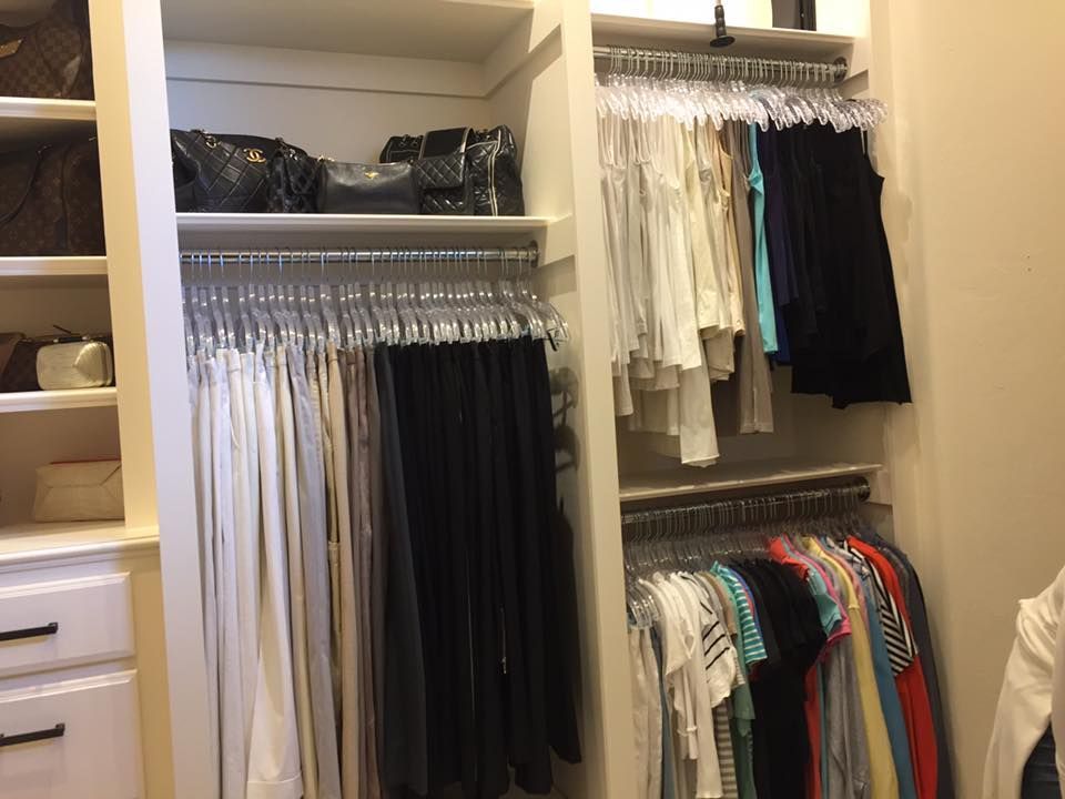 Closet with hanging clothes and purses on a top shelf. Various colors of clothing are visible.
