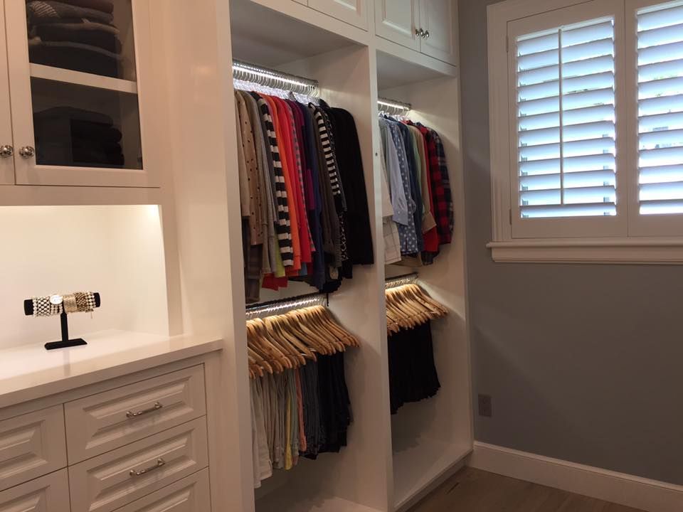 Walk-in closet with clothes on hangers and a window with white shutters.