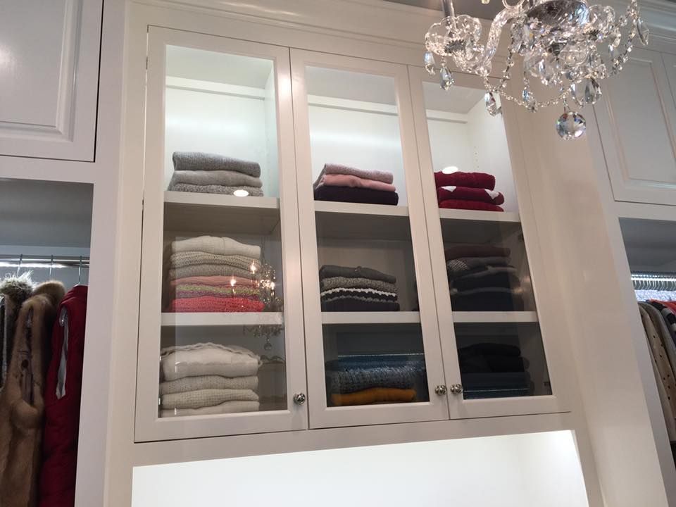 White cabinet with glass doors, showcasing folded sweaters in various colors.