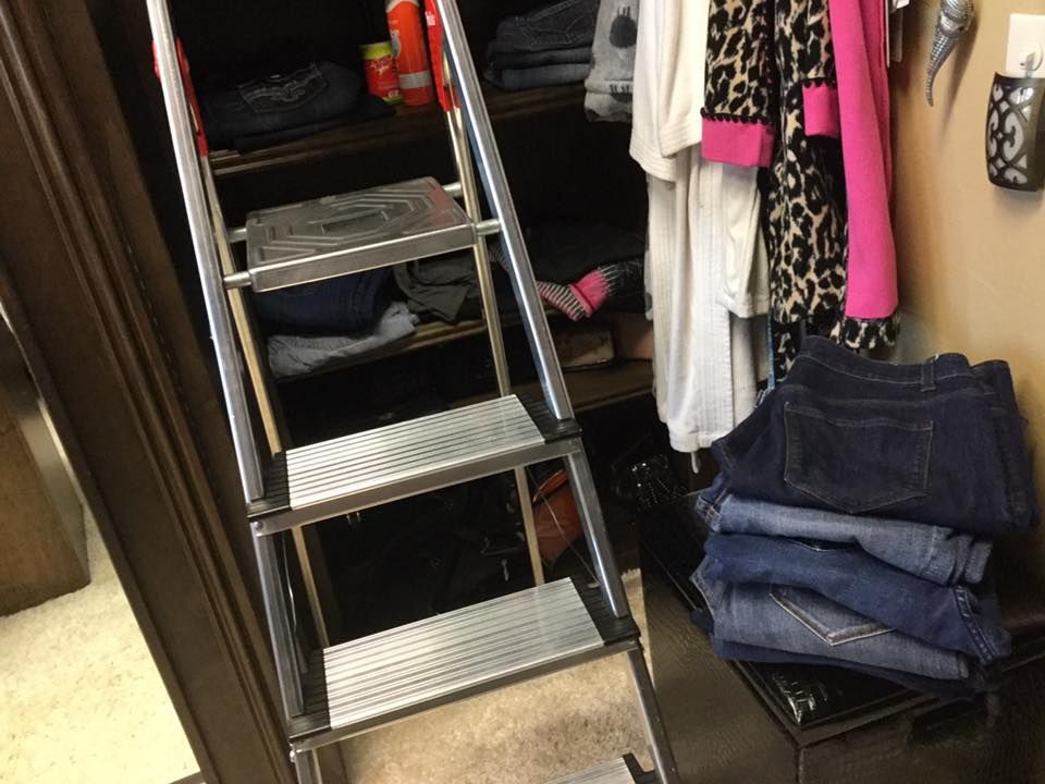 Ladder inside a closet, reaching upper shelves. Jeans stacked next to the ladder. Clothes hang on the right.