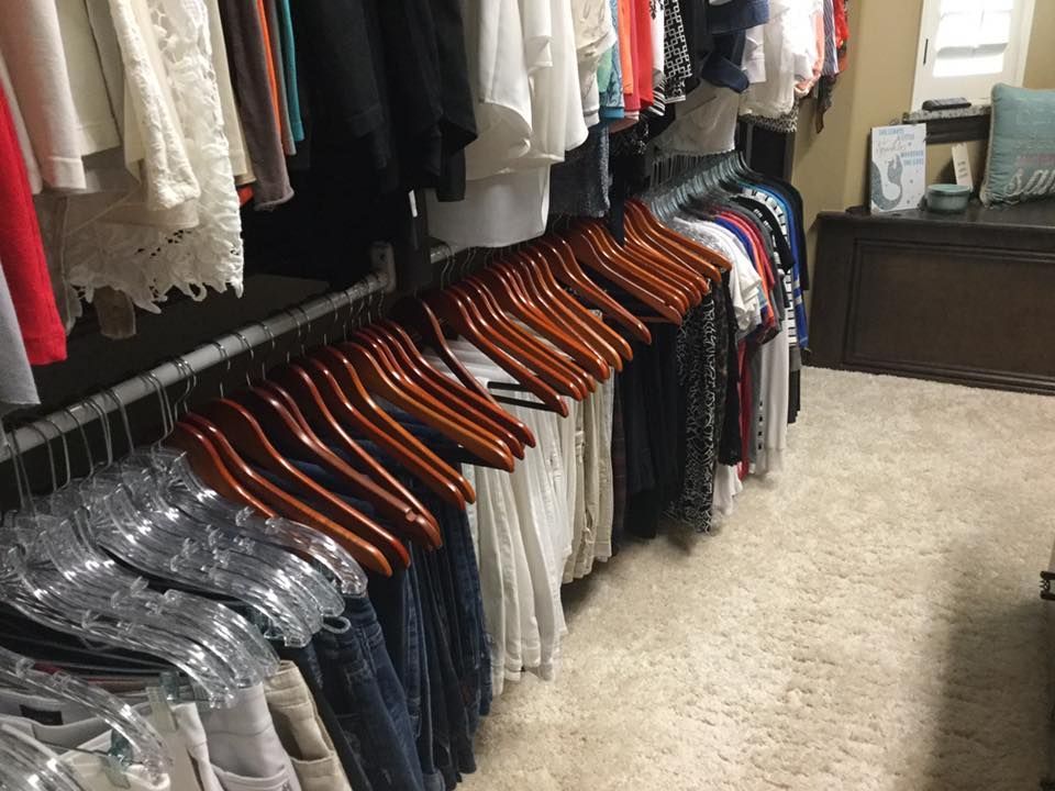 Closet with clothes on hangers. Brown and silver hangers with a variety of tops and pants hanging.