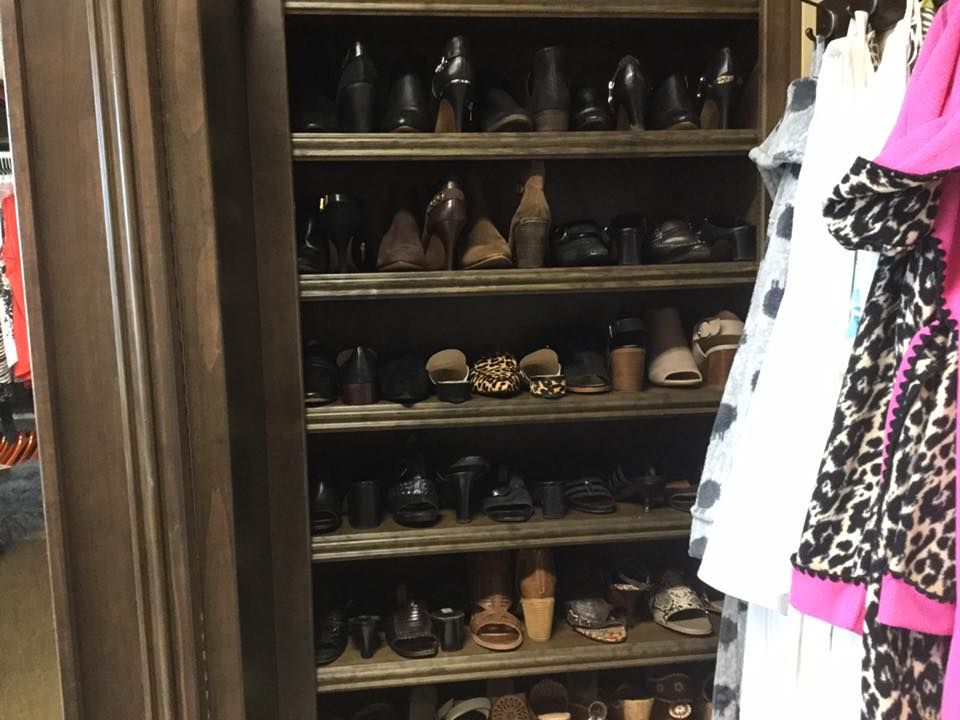 Wooden shoe rack filled with various shoes, next to a rack of clothes in a closet.