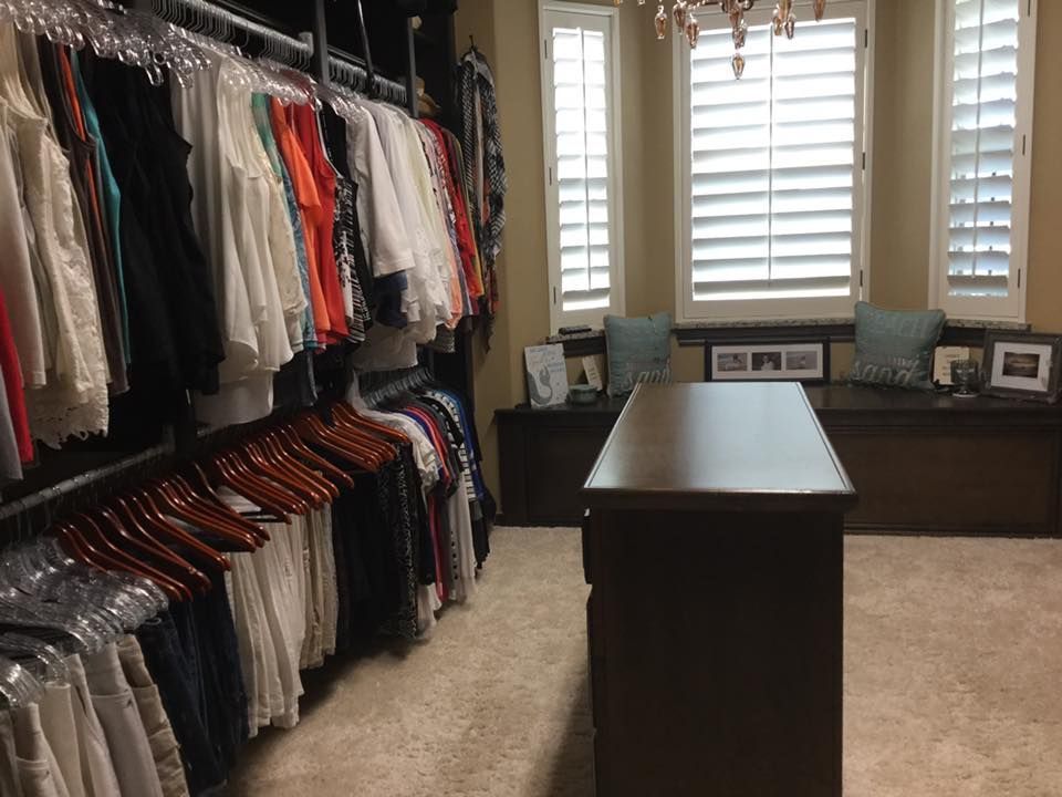 Walk-in closet with hanging clothes. A dark brown island is in front of a window with shutters and built-in seating.