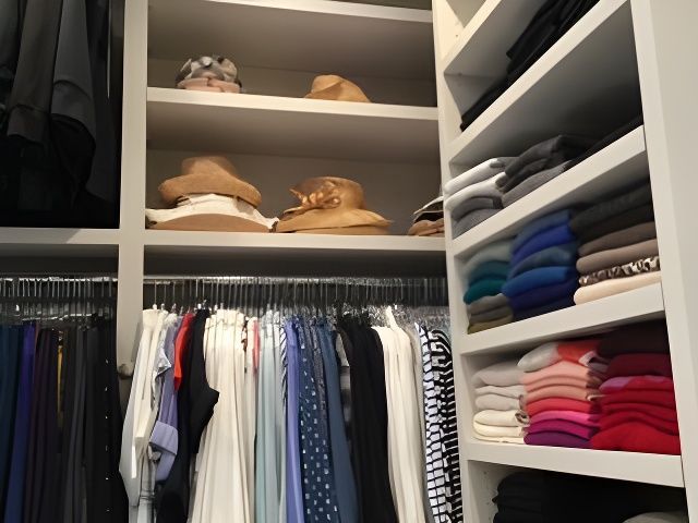Closet with neatly organized clothes: hanging garments, folded sweaters, and hats on shelves.
