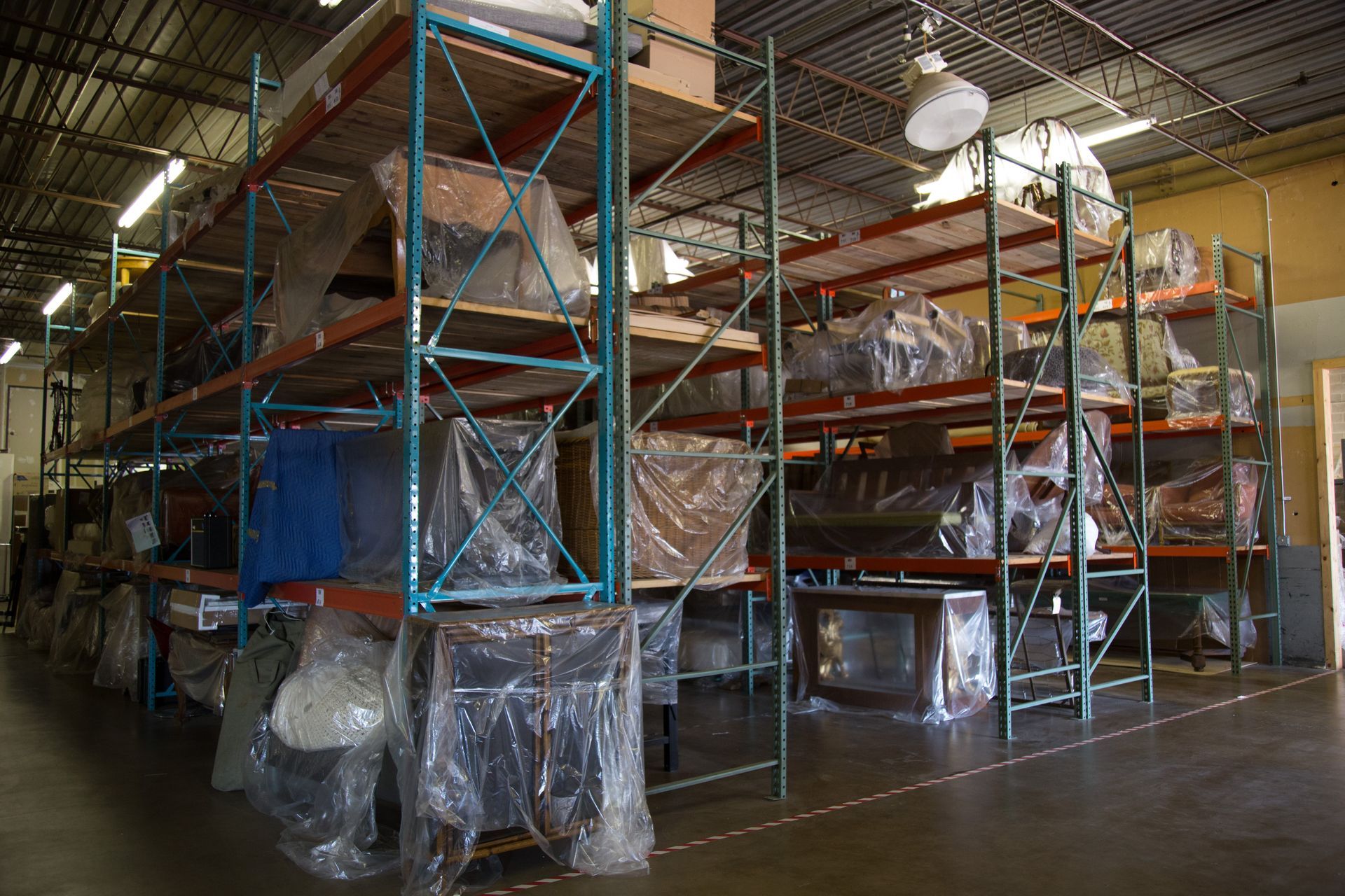 Warehouse with metal shelving, holding numerous items wrapped in clear plastic.