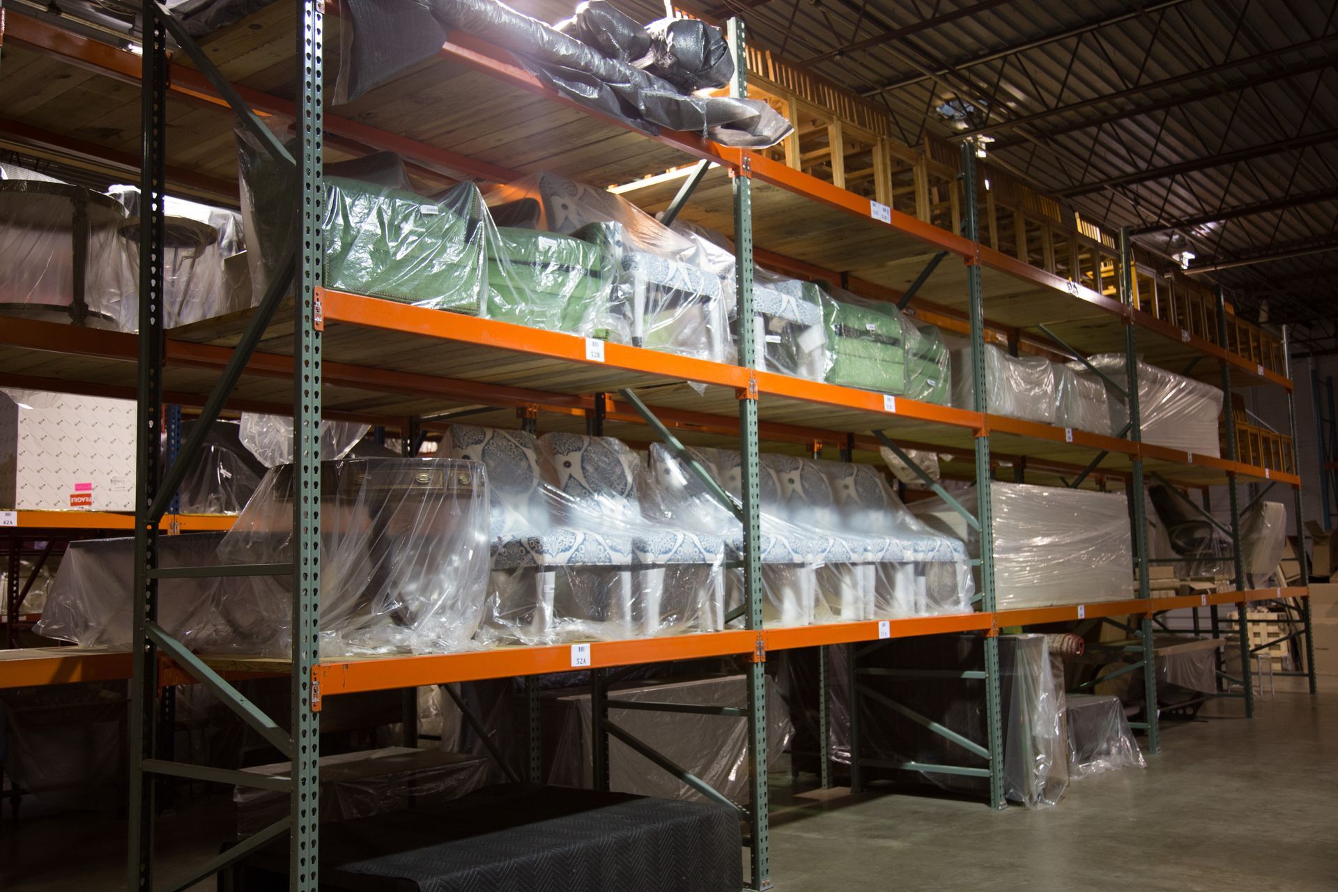 Warehouse shelves filled with wrapped machinery and equipment, lit by overhead lights.