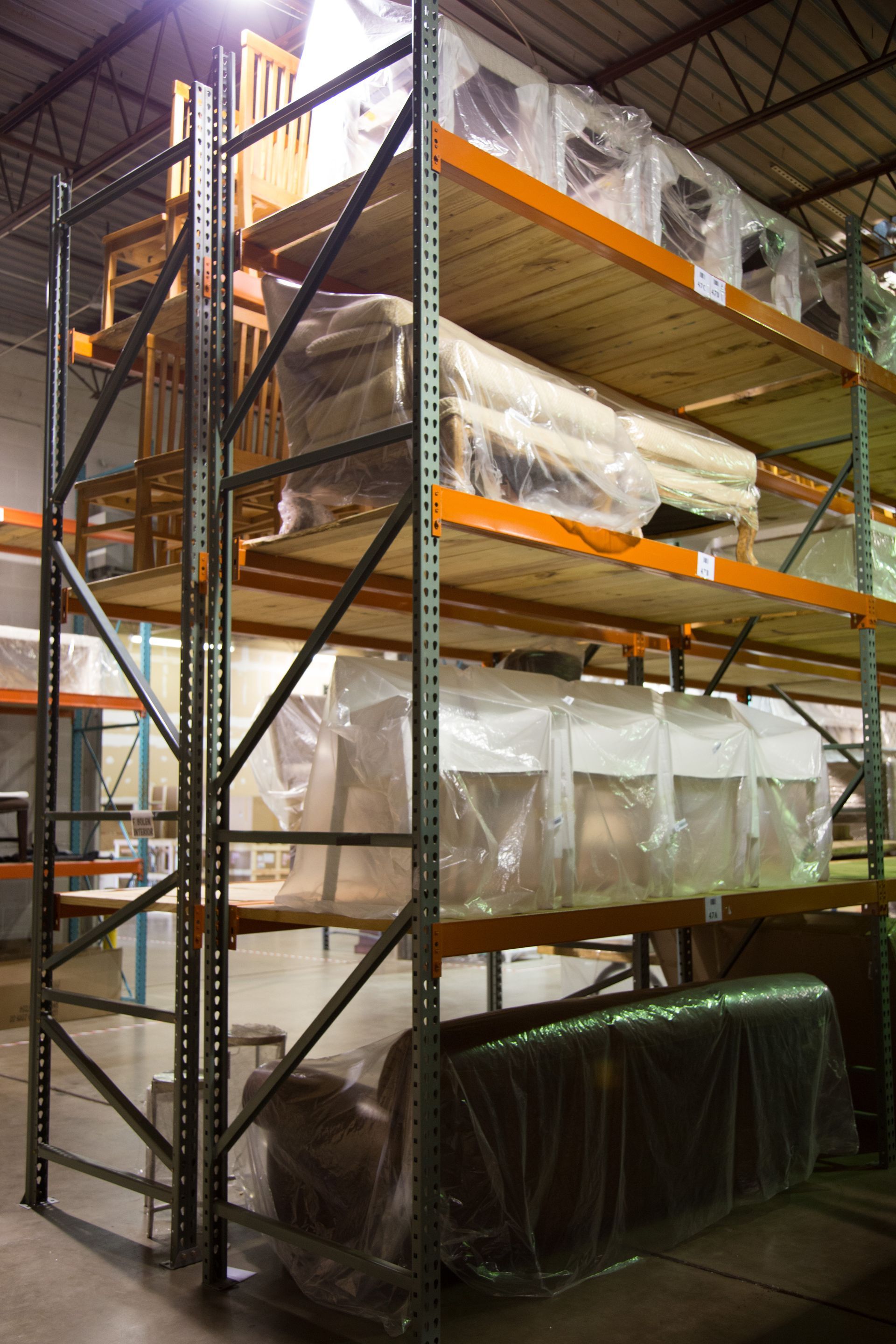 Metal storage rack in a warehouse, holding furniture wrapped in plastic.