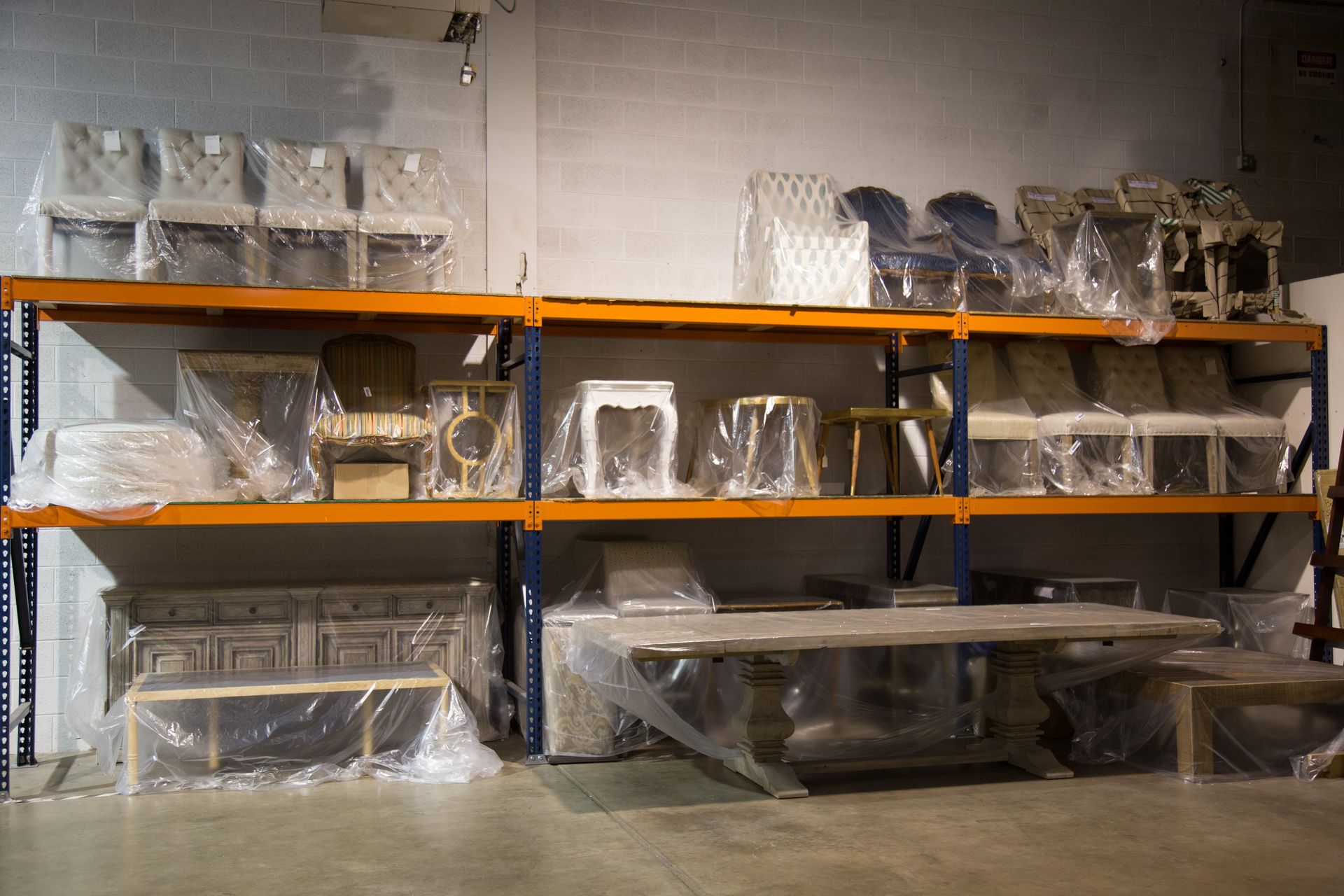 Shelves filled with wrapped furniture in a warehouse; includes chairs, tables, and a cabinet.