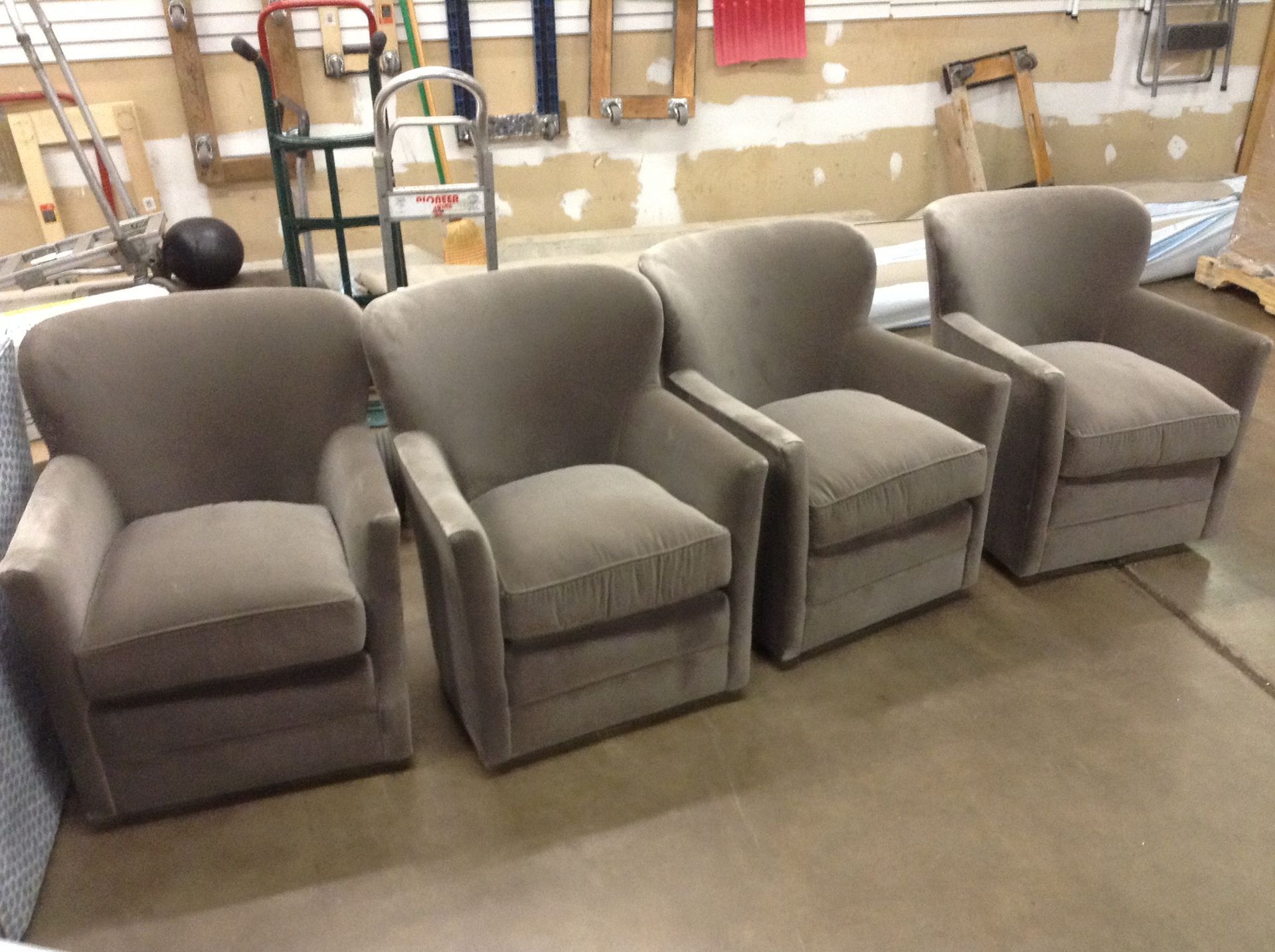 Four gray upholstered armchairs in a workshop, arranged side by side on a concrete floor.