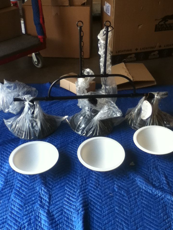 Black three-light fixture with white bowl shades, on a blue pad, surrounded by boxes.