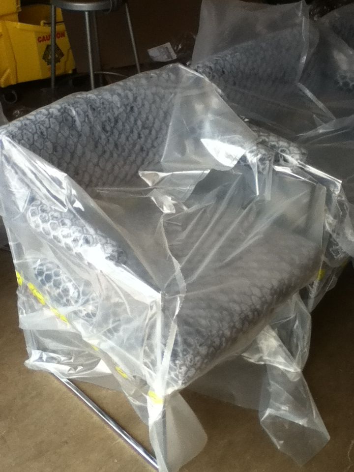 Armchair wrapped in clear plastic. Gray quilted seat and back on silver legs.