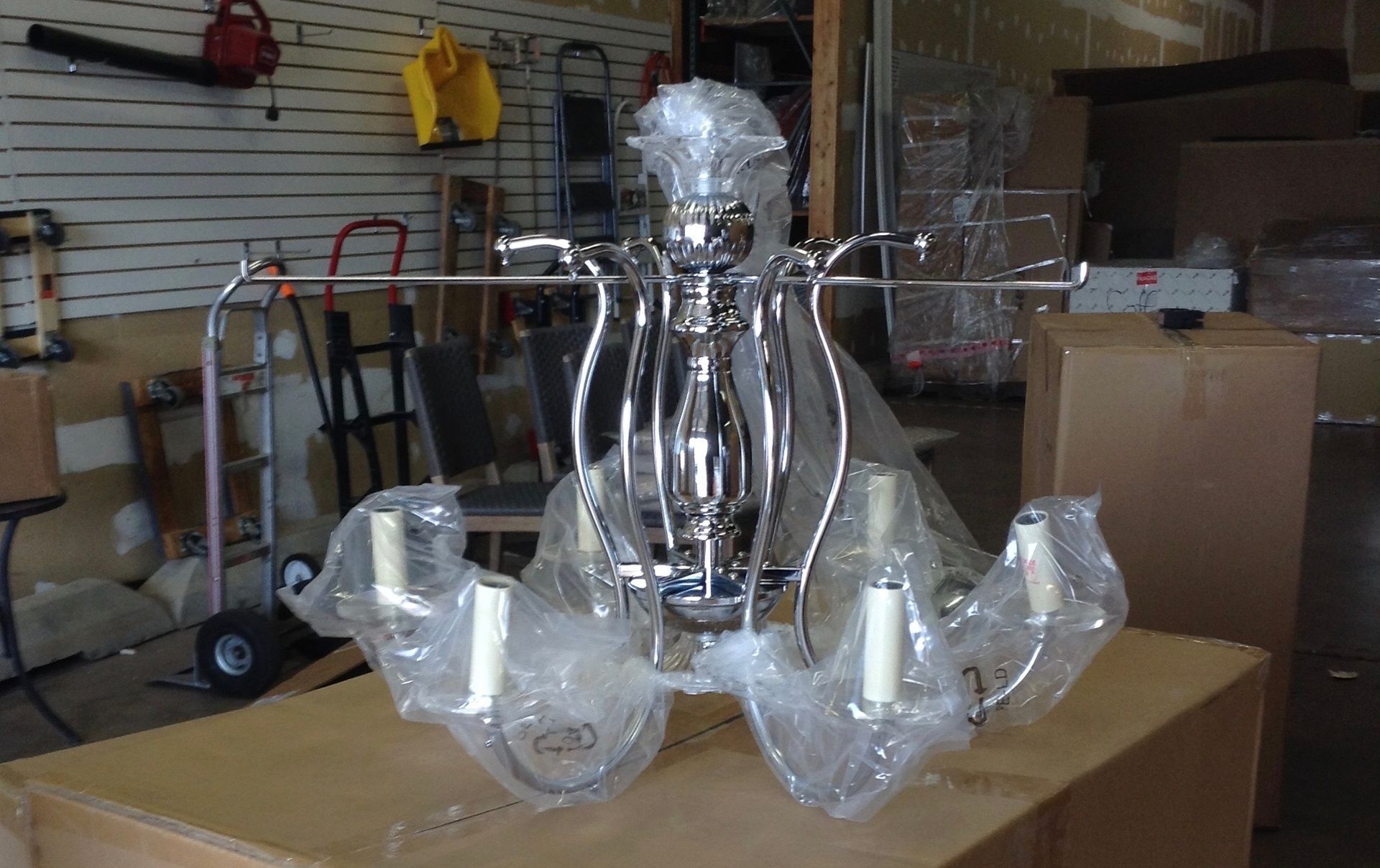 Chrome chandelier, wrapped in plastic, on a cardboard box in a warehouse.