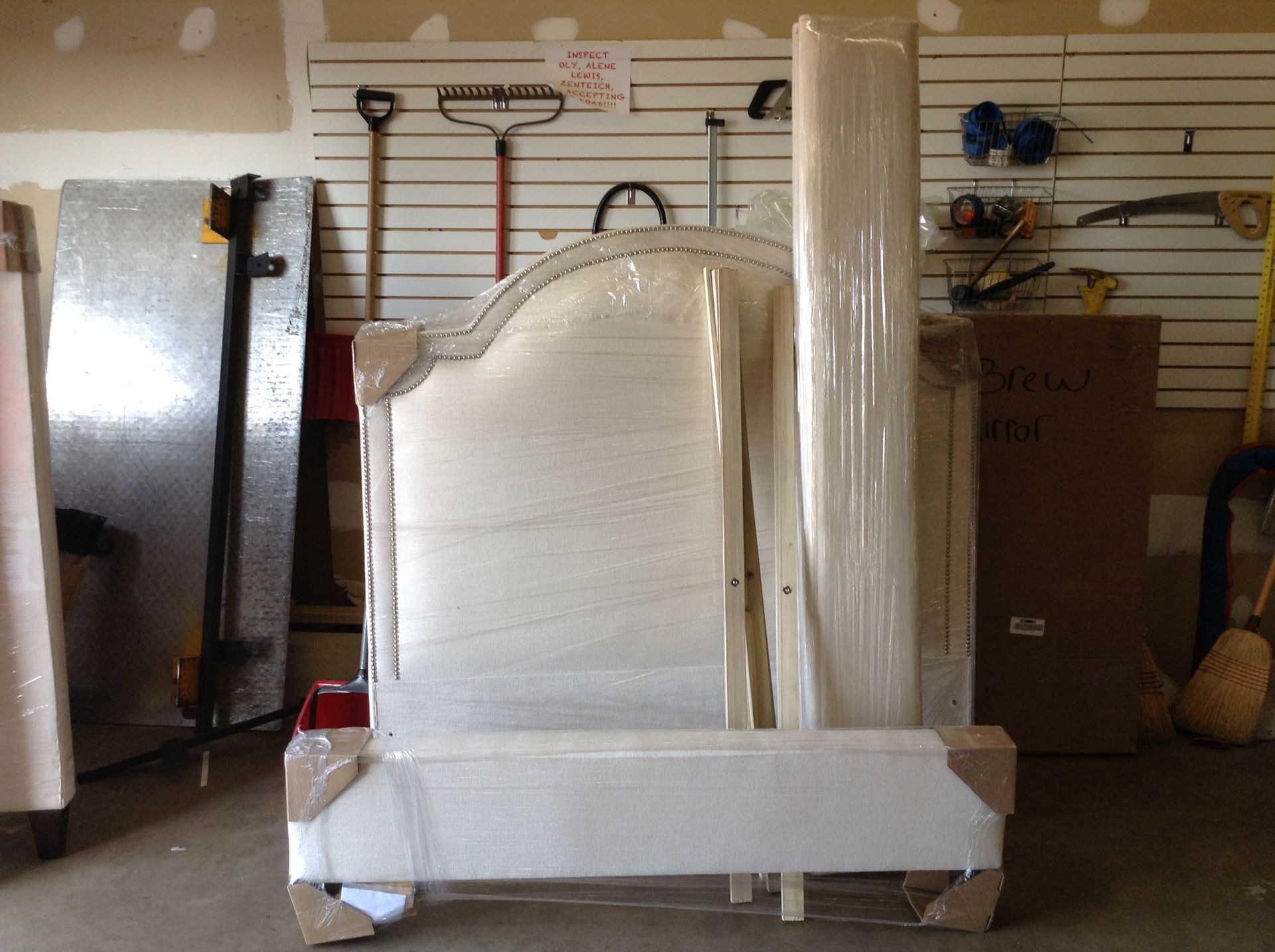 Wrapped bedroom furniture in a garage, ready for moving. Includes headboard, footboard, and side rails.