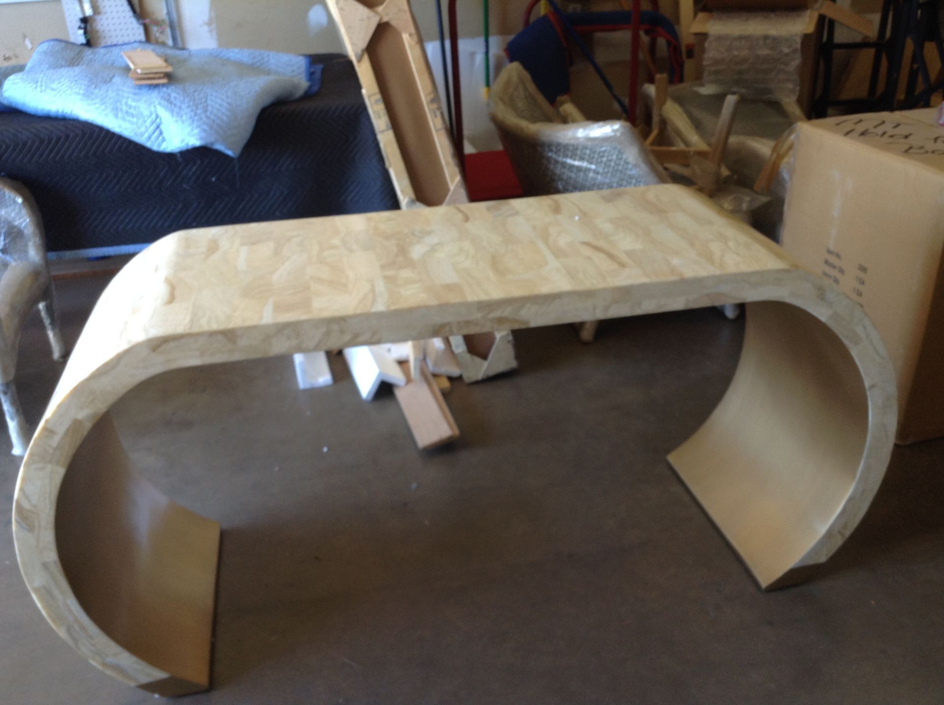 Light-colored, curved desk in a room with furniture and boxes.