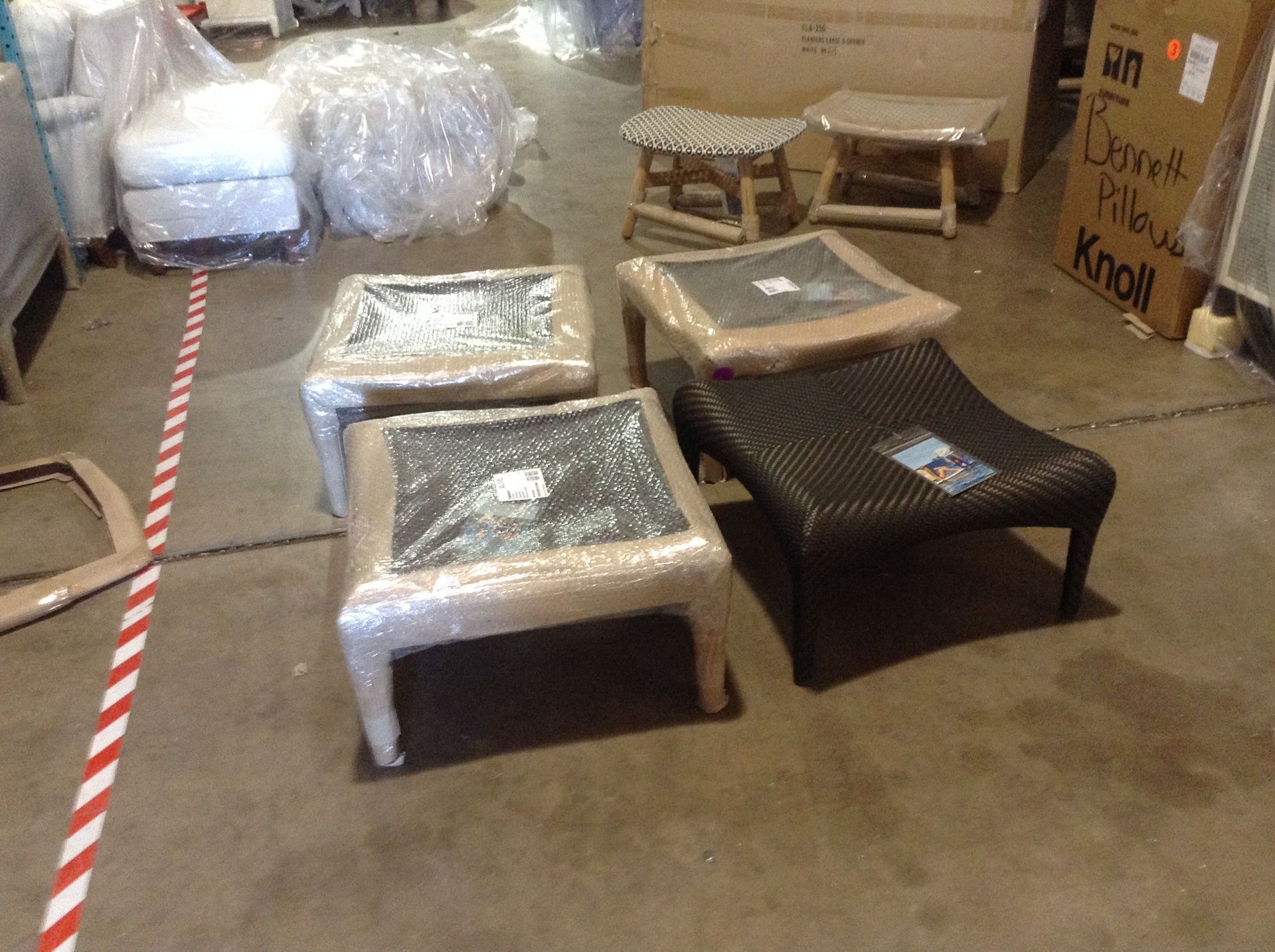 Four wrapped ottomans and two small stools on a warehouse floor.