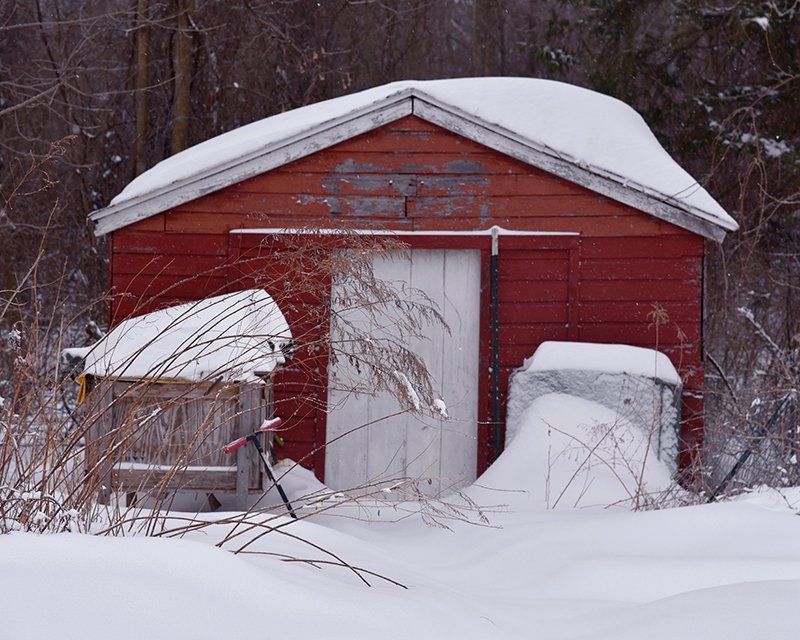 A red barn with a white door is covered in snow