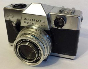 An instamatic reflex camera is sitting on a white surface