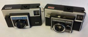 Two old cameras are sitting next to each other on a table.