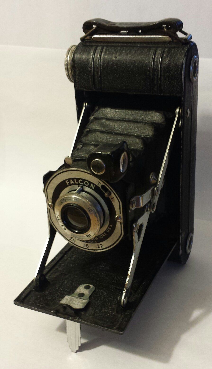 An old fashioned folding camera is sitting on a white surface.