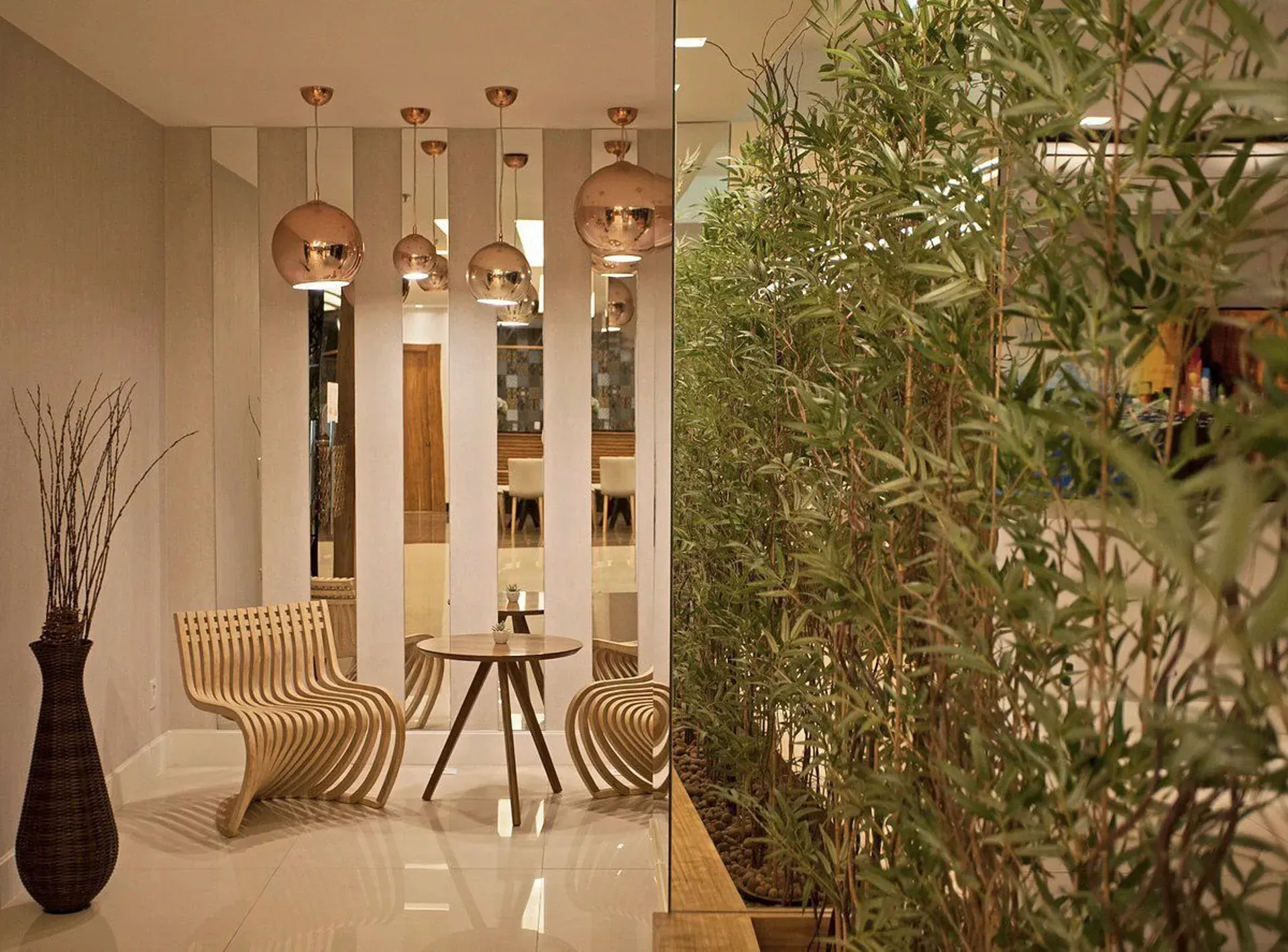 Sala de estar moderna e elegante com cadeiras de vime, luminárias pendentes e plantas altas de bambu em tons neutros.