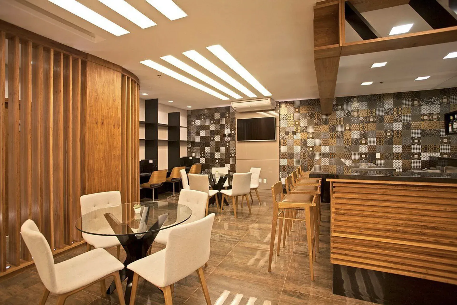 Interior de restaurante moderno com cadeiras brancas, detalhes em madeira e paredes revestidas com azulejos de mosaico.
