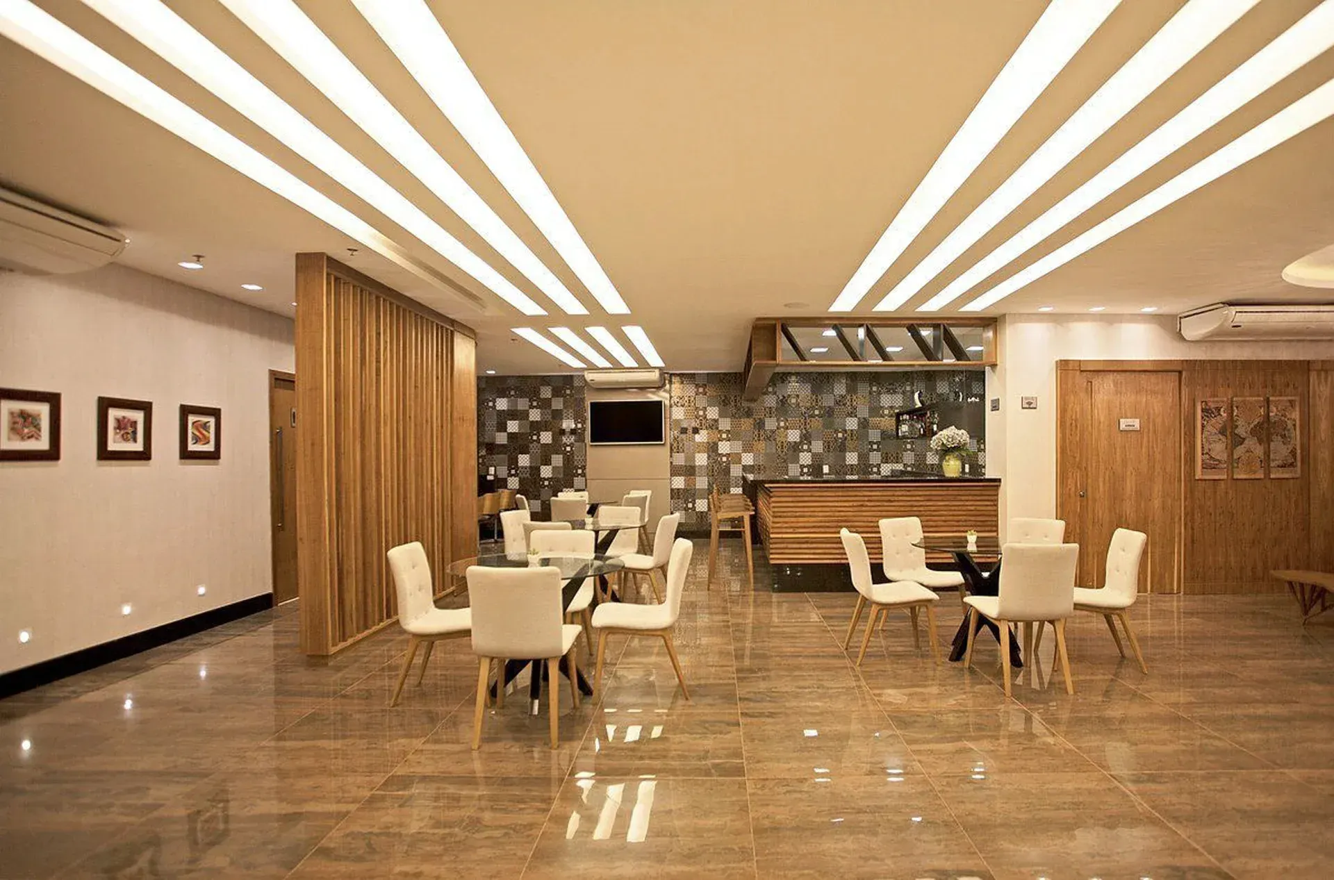 Elegante sala de estar de hotel com piso de mármore, cadeiras cor creme e um bar de madeira sob iluminação aconchegante.