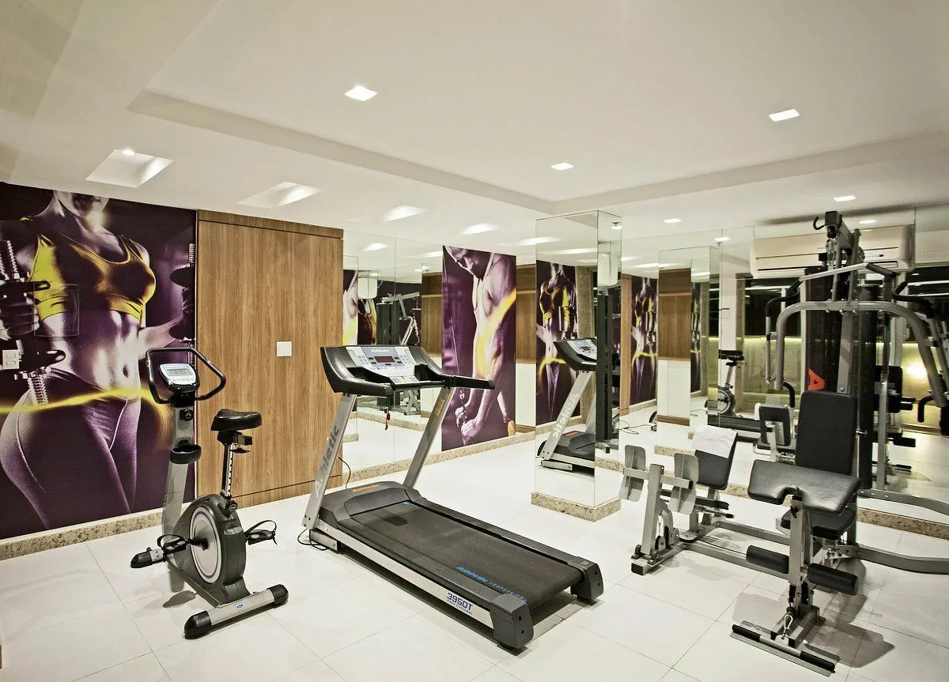 Interior de academia moderna com esteira, bicicletas ergométricas e aparelhos de musculação em uma sala espelhada.