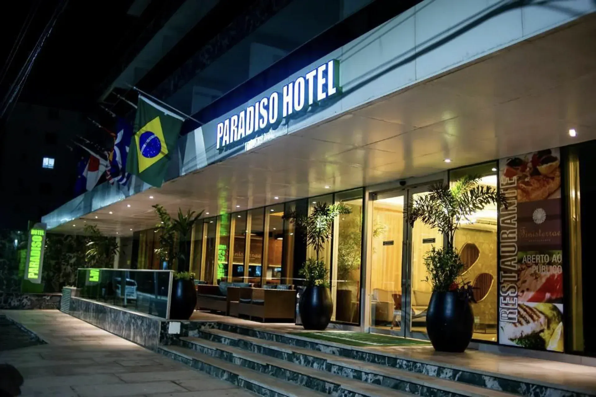 Exterior do Hotel Gards à noite, com entrada iluminada e fachada de vidro.