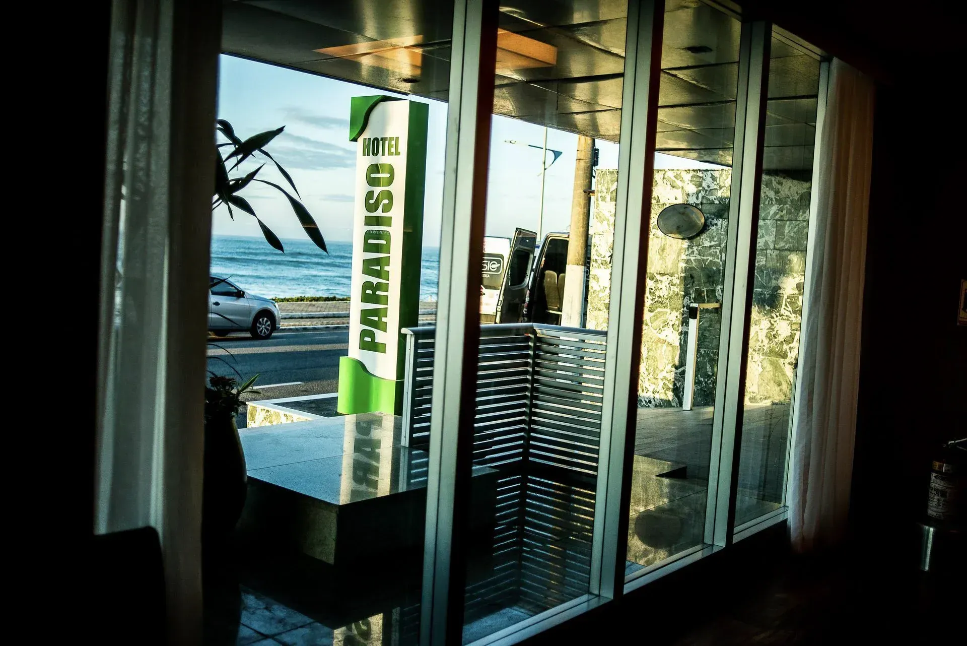 Vitrines com vista para a praia, com uma placa vertical verde escrito “PARADISE” no interior.