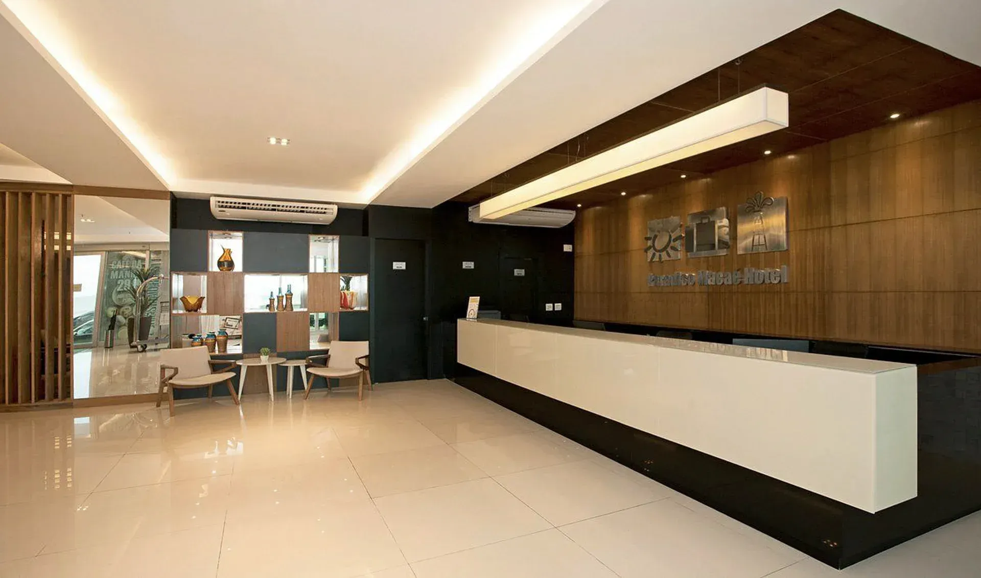 Hall de entrada moderno do hotel com balcão de recepção, parede com painéis de madeira e área de estar.